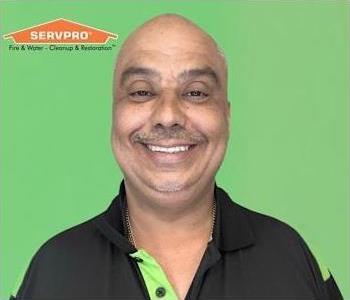 Man in polo shirt in front of green background with orange logo in top left.